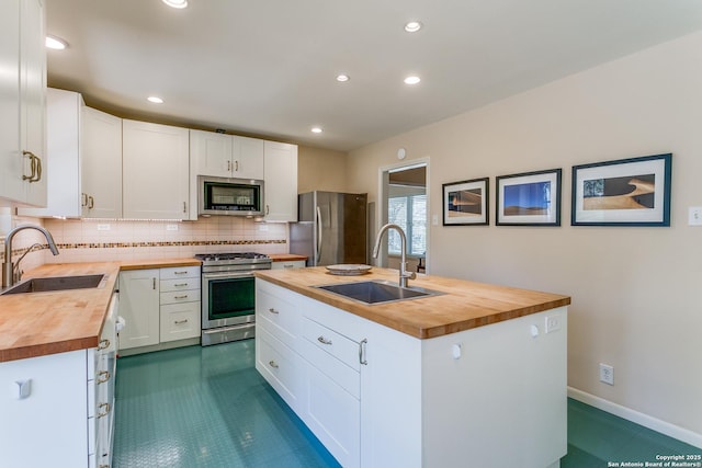 kitchen with a kitchen island with sink, stainless steel appliances, wood counters, and a sink
