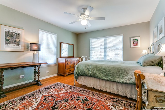bedroom with ceiling fan, baseboards, multiple windows, and wood finished floors