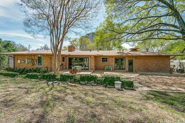 rear view of house with a patio area, french doors, a chimney, and brick siding