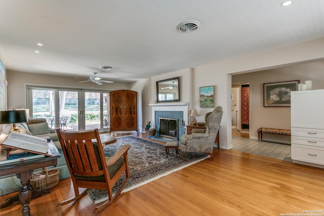 living area featuring light wood-type flooring, visible vents, a fireplace, baseboards, and ceiling fan
