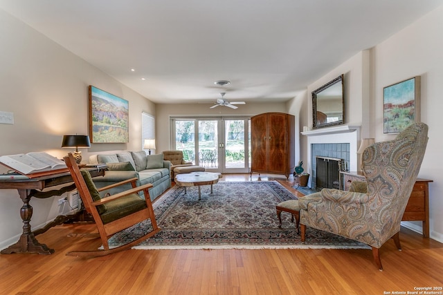 living area with a tiled fireplace, baseboards, ceiling fan, and wood-type flooring