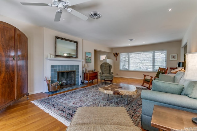 living room featuring light wood finished floors, visible vents, a tiled fireplace, and ceiling fan