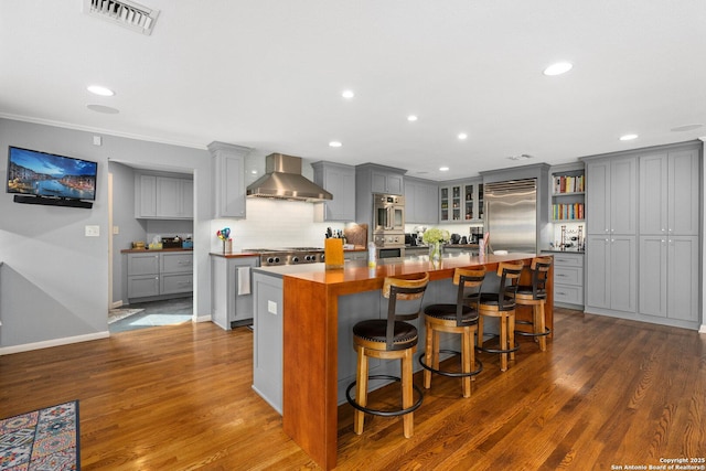 kitchen featuring visible vents, gray cabinets, a kitchen island, stainless steel appliances, and wall chimney range hood