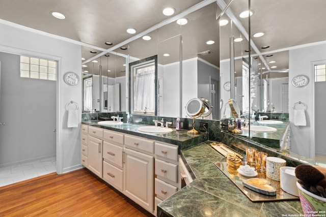 bathroom featuring wood finished floors, visible vents, double vanity, ornamental molding, and a sink