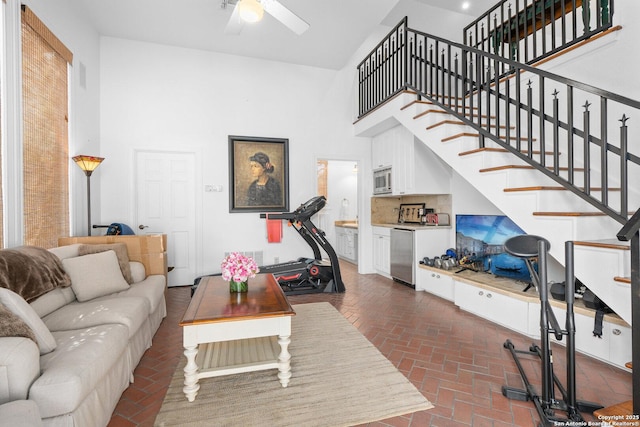 living area featuring ceiling fan, brick floor, stairs, and a towering ceiling