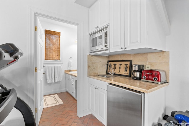 kitchen featuring a sink, stainless steel microwave, white cabinets, decorative backsplash, and dishwasher