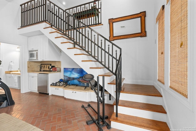 staircase featuring brick floor, baseboards, and a towering ceiling