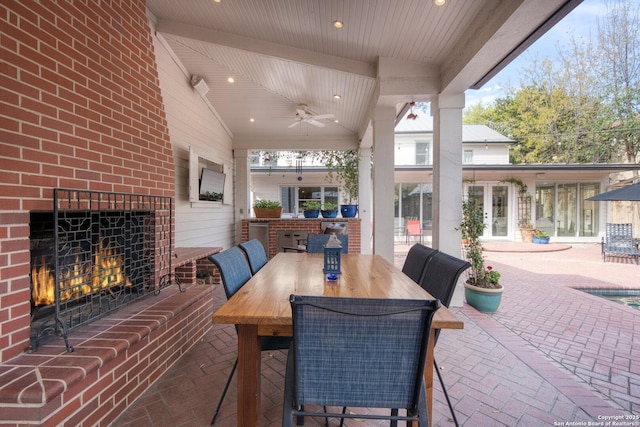 view of patio / terrace featuring outdoor dining area, french doors, a ceiling fan, and an outdoor brick fireplace