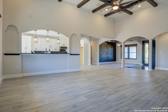 116 Hidden Ranch Ct, Floresville, TX 78114 - unfurnished living room with beamed ceiling, a towering ceiling, arched walkways, baseboards, and light wood-style floors