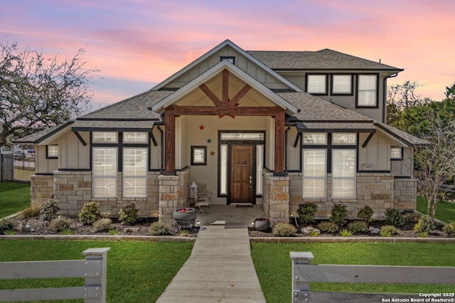 view of front of house featuring stone siding, fence, board and batten siding, and a shingled roof