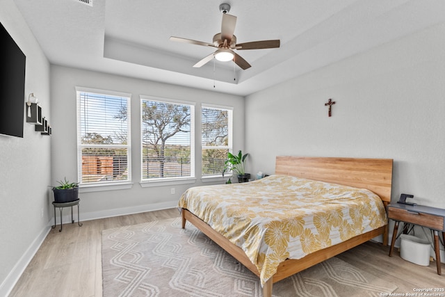 bedroom with a tray ceiling, light wood-style flooring, baseboards, and ceiling fan