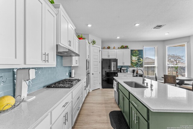 kitchen with green cabinets, under cabinet range hood, stainless steel gas cooktop, white cabinets, and a sink