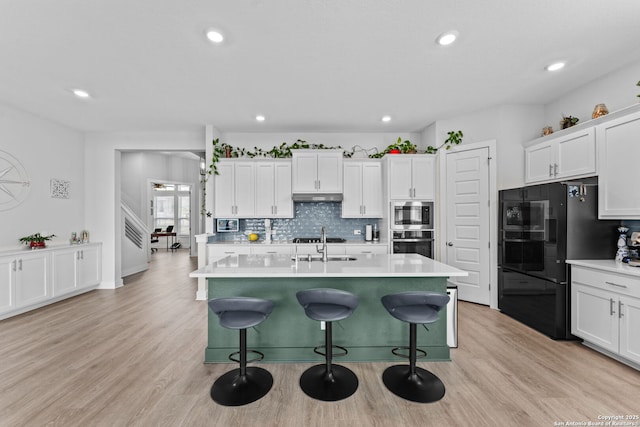 kitchen with under cabinet range hood, appliances with stainless steel finishes, white cabinets, and light wood finished floors