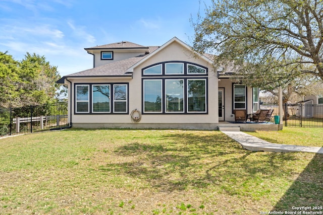 rear view of house with stucco siding, a lawn, fence private yard, and a shingled roof