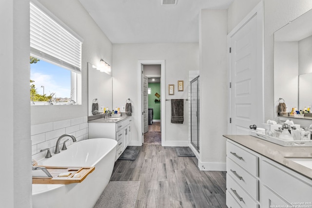 bathroom featuring wood finished floors, visible vents, two vanities, a stall shower, and a freestanding bath