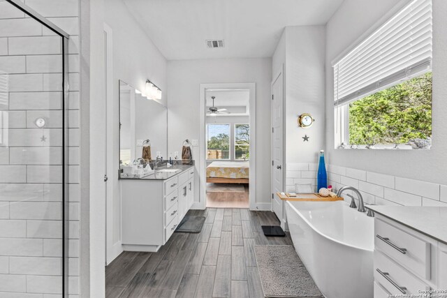 ensuite bathroom featuring vanity, wood finished floors, visible vents, a freestanding bath, and connected bathroom