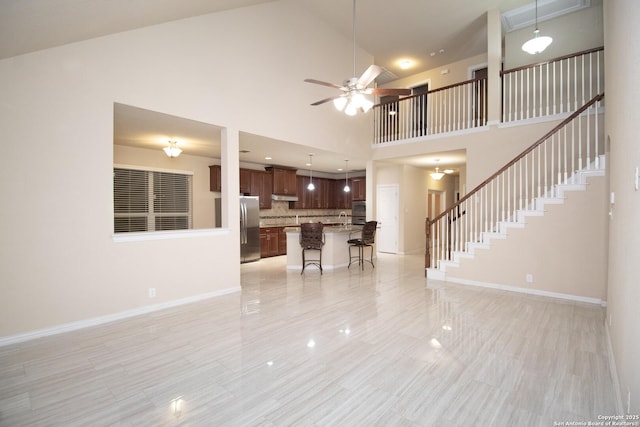 living room with stairway, baseboards, a high ceiling, and a ceiling fan