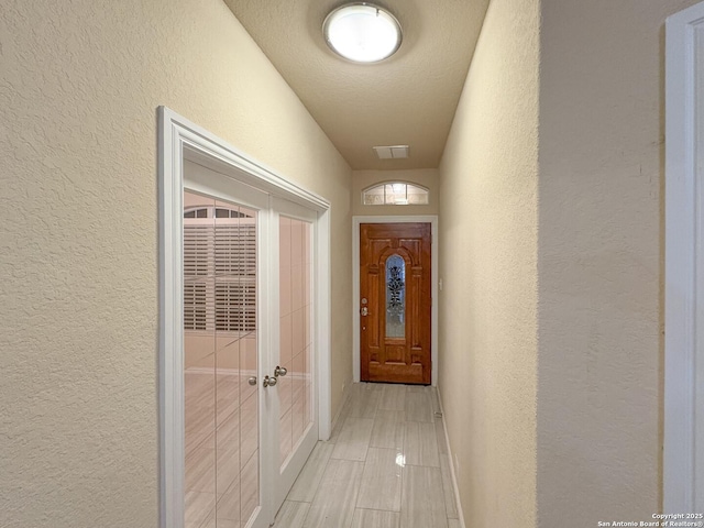 hallway featuring visible vents, a textured ceiling, and a textured wall