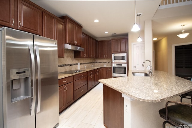 kitchen with a breakfast bar, a sink, stainless steel appliances, under cabinet range hood, and tasteful backsplash