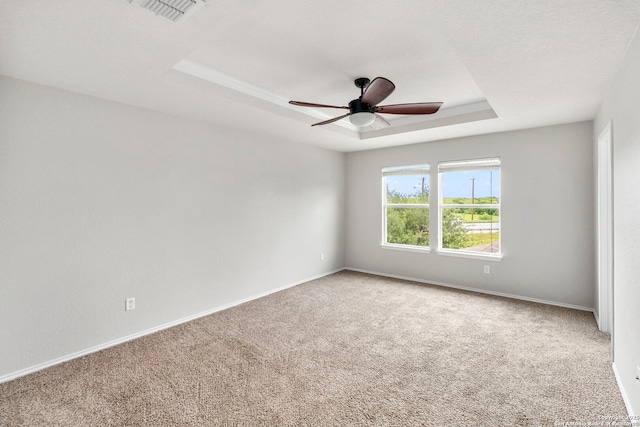 empty room with visible vents, a raised ceiling, a ceiling fan, and carpet flooring