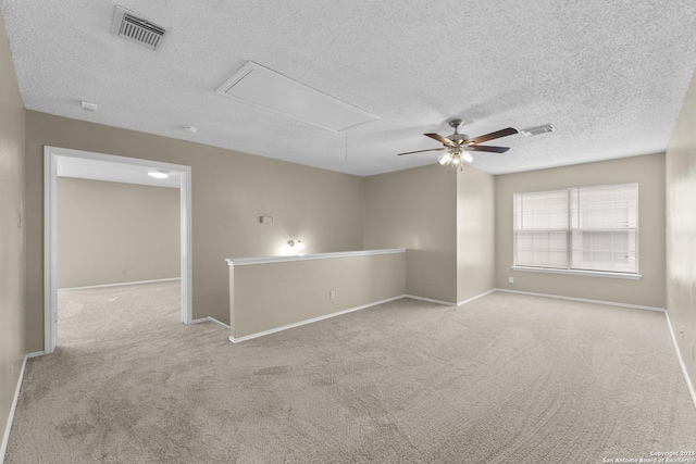 carpeted spare room featuring visible vents, attic access, a textured ceiling, and ceiling fan