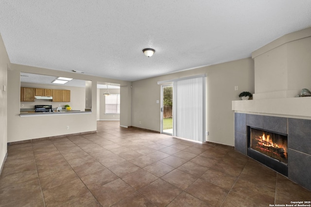 unfurnished living room featuring a tiled fireplace, baseboards, tile patterned floors, and a textured ceiling
