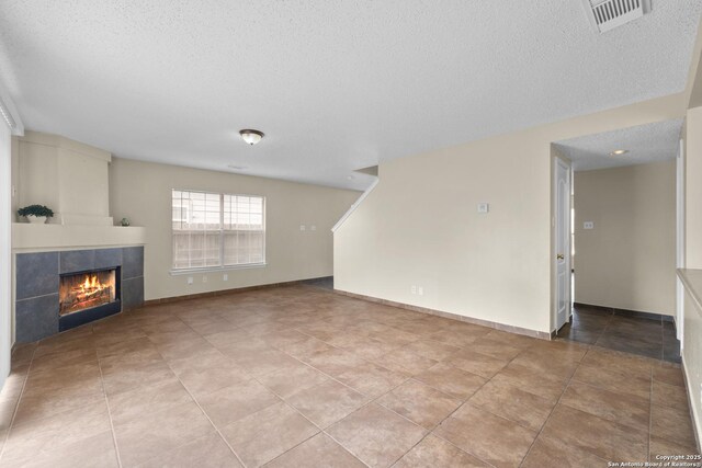 unfurnished living room featuring visible vents, a textured ceiling, baseboards, and a tile fireplace