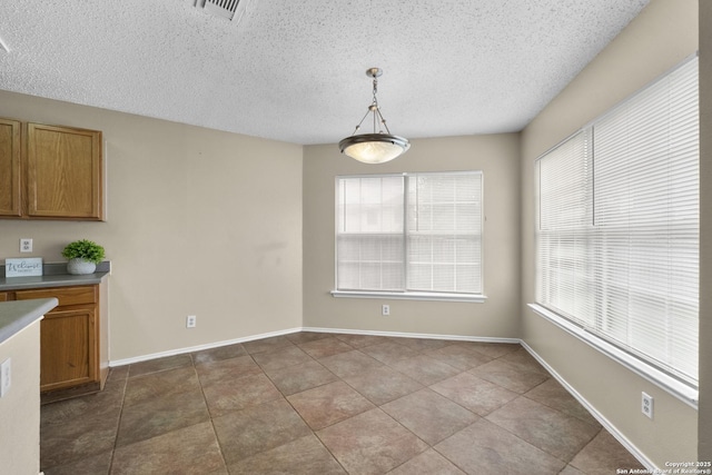 unfurnished dining area featuring plenty of natural light, a textured ceiling, and visible vents