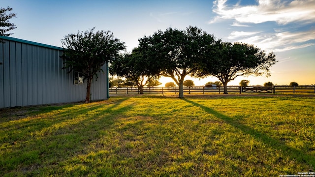 yard at dusk with a rural view, an outbuilding, and fence