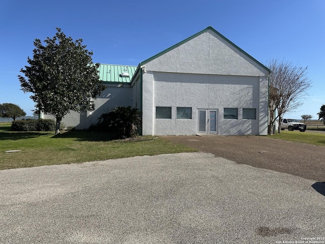 view of property exterior with stucco siding, a yard, metal roof, and french doors
