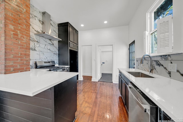 kitchen featuring a sink, wall chimney range hood, wood-type flooring, appliances with stainless steel finishes, and light countertops