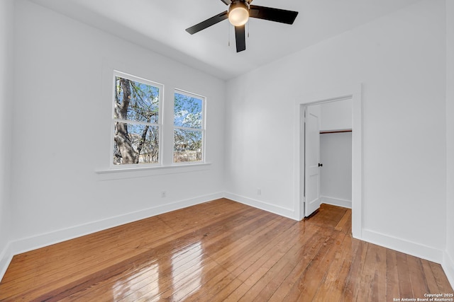 unfurnished bedroom featuring a walk in closet, ceiling fan, baseboards, a closet, and wood-type flooring