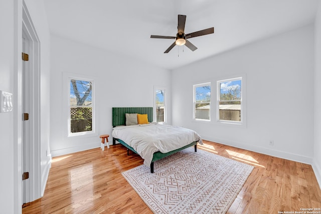 bedroom with baseboards, multiple windows, light wood-style floors, and a ceiling fan
