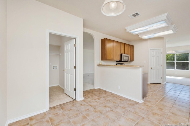 14204 Auberry, Helotes, TX 78023 - kitchen with stainless steel microwave, brown cabinets, arched walkways, light countertops, and light tile patterned floors