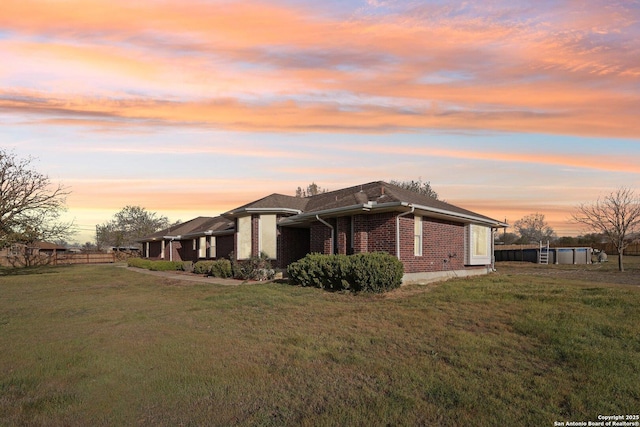 view of side of home featuring brick siding, a lawn, and fence