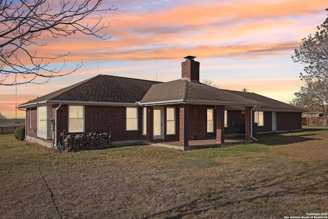 view of front of property featuring a yard, roof with shingles, brick siding, a chimney, and a patio area