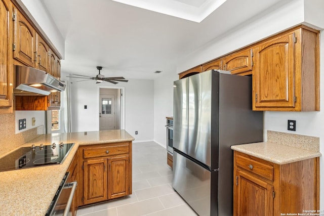 kitchen with freestanding refrigerator, oven, under cabinet range hood, black electric stovetop, and brown cabinets
