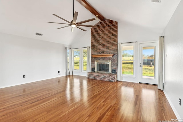 unfurnished living room with visible vents, a healthy amount of sunlight, beam ceiling, wood finished floors, and a ceiling fan
