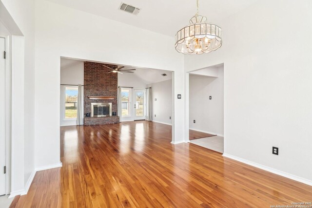 unfurnished living room featuring visible vents, a brick fireplace, baseboards, light wood-style flooring, and ceiling fan with notable chandelier