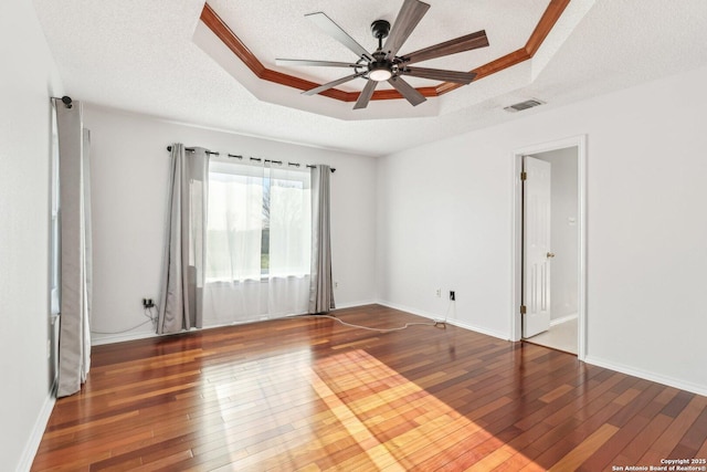 empty room with a tray ceiling, visible vents, hardwood / wood-style floors, and a ceiling fan