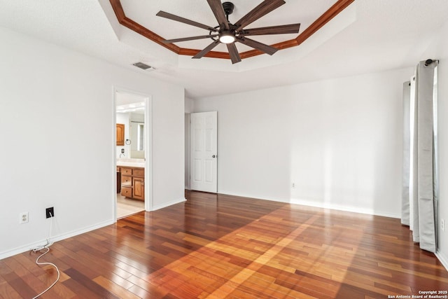 unfurnished bedroom featuring visible vents, crown molding, baseboards, a tray ceiling, and hardwood / wood-style floors