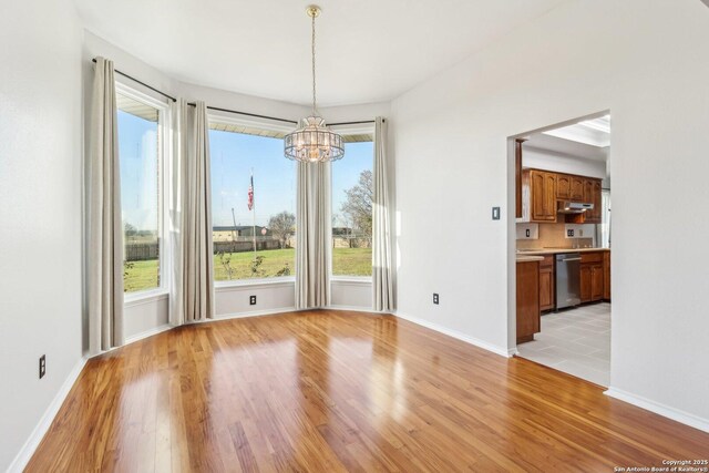 unfurnished dining area featuring light wood finished floors, baseboards, and an inviting chandelier
