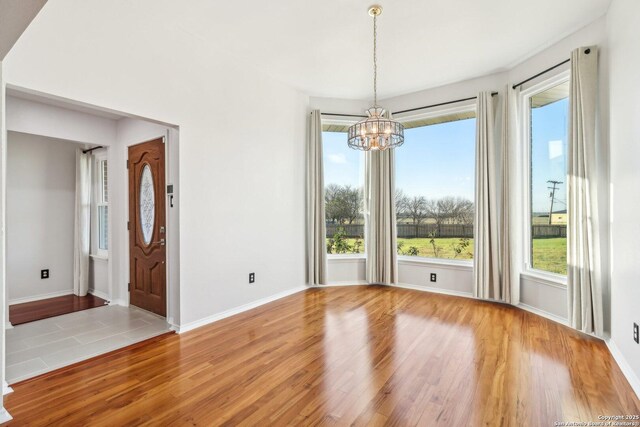 empty room with a chandelier, baseboards, and wood finished floors