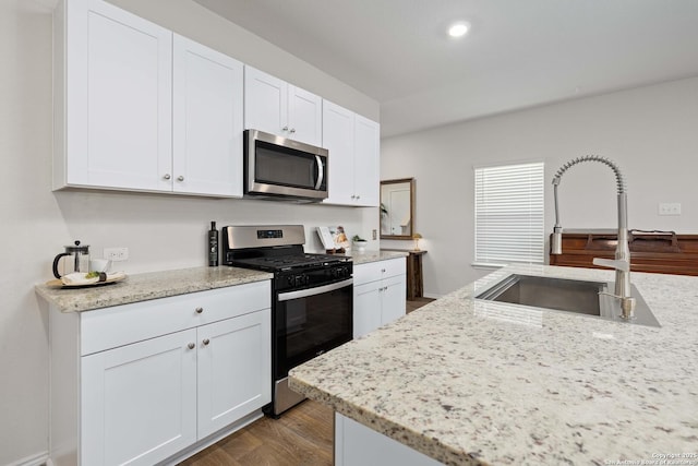 kitchen with recessed lighting, wood finished floors, white cabinets, stainless steel appliances, and a sink
