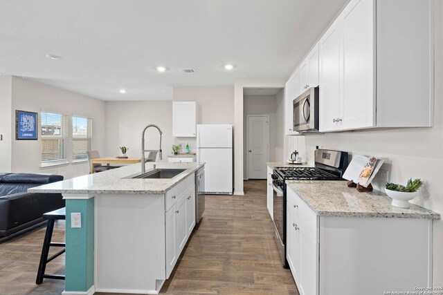 kitchen featuring open floor plan, appliances with stainless steel finishes, wood finished floors, white cabinets, and a sink