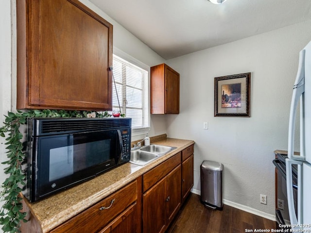 kitchen with dark wood-type flooring, black appliances, a sink, light countertops, and baseboards