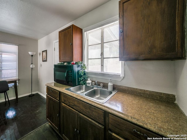 kitchen featuring dark wood-type flooring, a sink, a textured ceiling, black microwave, and baseboards