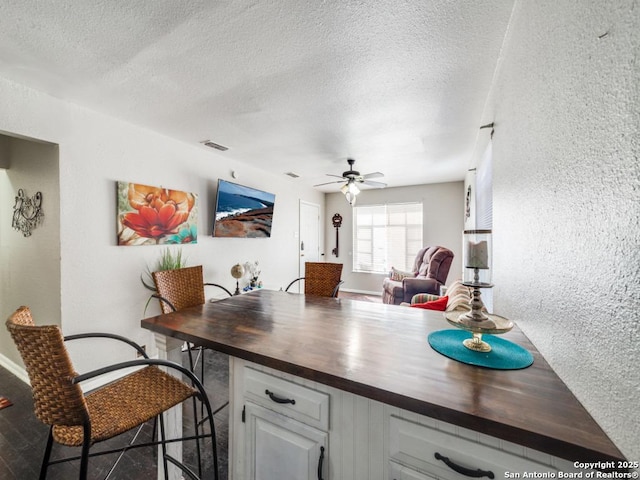 kitchen with visible vents, wooden counters, a ceiling fan, and a textured wall