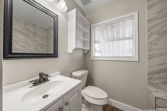 bathroom with visible vents, baseboards, toilet, a textured wall, and vanity