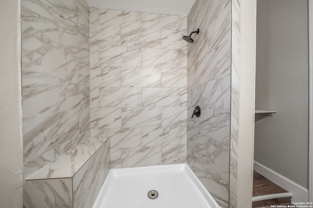 full bathroom with tiled shower and baseboards